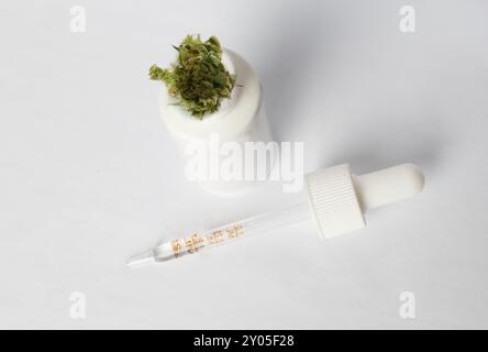 Primo piano di una bottiglia contagocce bianca per olio di cannabis con pianta di marijuana su sfondo bianco, vista dall'alto. Prodotto in bottiglia di olio di canapa CBD e THC Foto Stock