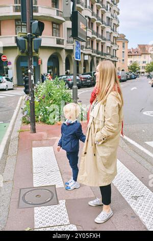 La giovane madre e il piccolo figlio aspettano il via libera per attraversare la strada Foto Stock