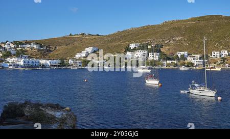 Vista delle barche a vela che si stendono tranquillamente nel mare blu al largo di una città costiera sotto un cielo azzurro, del porto di Grikos, di Grikos, di Patmos, del Dodecaneso, isola greca Foto Stock