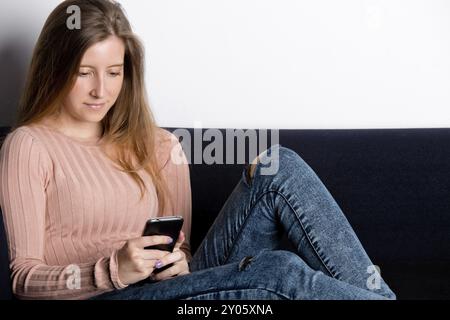 Felice donna seduta su un divano e utilizzando un telefono cellulare Foto Stock