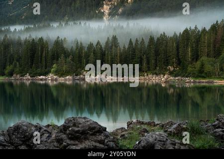 Vista panoramica mattutina sul Lago di Fusine vicino al confine tra Italia e Slovenia. Incantevole lago con incredibili acque profonde e colorate e foresta nebbiosa intorno. Foto Stock