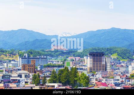 Teleobiettivo della città di Takayama, della sede centrale mondiale di Sukyo Mahikari e della catena montuosa innevata a strati sotto un cielo leggermente nuvoloso a Gifu Pr Foto Stock