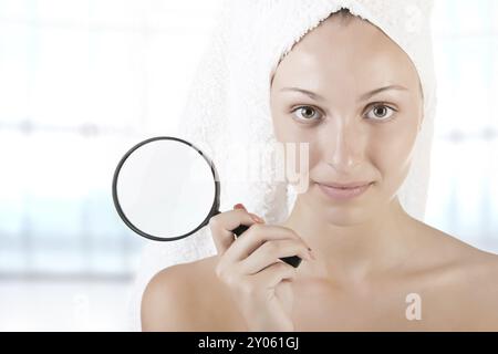 Donna con un asciugamano avvolto intorno alla testa tenendo una loupe, su sfondo blu Foto Stock