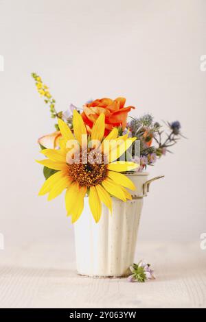 Mazzo di fiori freschi colorati collocato all'interno di una piccola piantatrice in ceramica sul tavolo contro la parete grigia Foto Stock