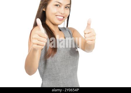 Una donna asiatica carina in abito grigio senza maniche che approva con due pollici in su, si concentra sui pollici che un lavoro ben fatto, accordo, complimento o approvazione. Foto Stock