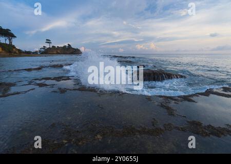 Un'onda si rompe sul bordo di una serie di piscine di marea durante un tramonto serale sull'idilliaca isola di Neil delle Andamane e delle Isole Nicobare in India Foto Stock