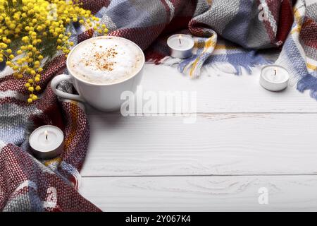 Cappuccino a caffè caldo, coperta, candele, fiori di mimosa su vecchio sfondo in legno. Concetto di relax romantico stagionale, in appartamento Foto Stock