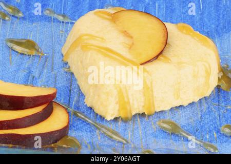 Dessert bavarese alla pesca a forma di cuore con salsa di pesca e fette di pesca su un piatto di vetro trasparente su sfondo blu Foto Stock