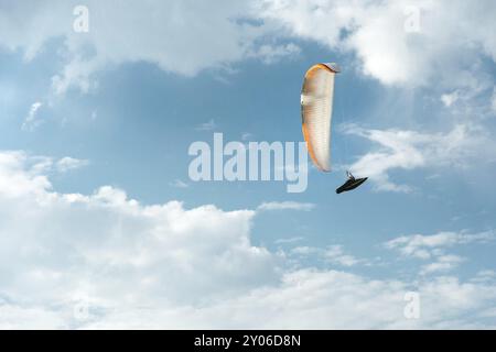 Il parapendio professionista vola su un parapendio bianco contro il cielo blu e le nuvole bianche. Sport di parapendio Foto Stock