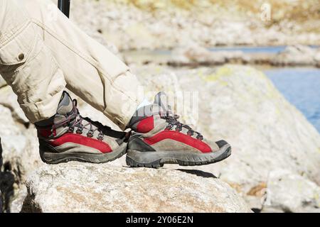 Una ragazza hipster sottile e graziosa con un berretto e una giacca rossa con uno zaino e un tappeto ripiegato per il relax si staglia in montagna sullo sfondo di Foto Stock