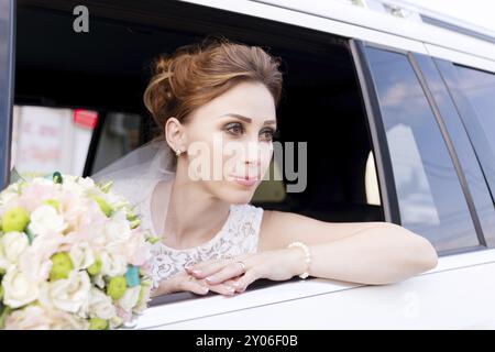 Ritratto ravvicinato di una splendida sposa accanto al suo bouquet di nozze nella finestra di una macchina da sposa. Il concetto di grazia nuziale Foto Stock