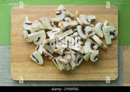 Primo piano di funghi tritati adagiati su un tagliere di legno su un tavolo da cucina verde. Il concetto di cucina a casa e vegetariana Foto Stock