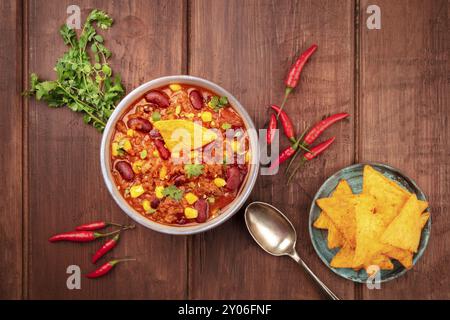 Chili con carne, ripresa dall'alto su una scuri in legno rustico sfondo con ingredienti e nachos Foto Stock