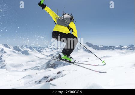 Uno sciatore con attrezzatura sportiva completa salta nell'abisso dalla cima del ghiacciaio sullo sfondo del cielo blu e del Caucaso innevato Foto Stock