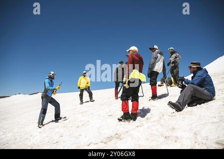 Allenamento per correggere lo scivolamento su un pendio o su un ghiacciaio con l'aiuto di un'ascia di ghiaccio. Una giovane guida con la barba spiega al suo gruppo come rallentare correttamente il Foto Stock