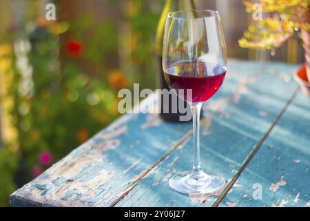 Un bicchiere di vino rosso su un vecchio tavolo rustico in legno. Godendole nel giardino privato al sole della sera Foto Stock