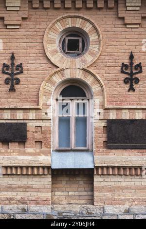 Finestra ad arco vintage nella parete di mattoni gialli. Vetro nero in una cornice in legno rosso scuro marrone. Il concetto di antica architettura vintage in costruzione Foto Stock