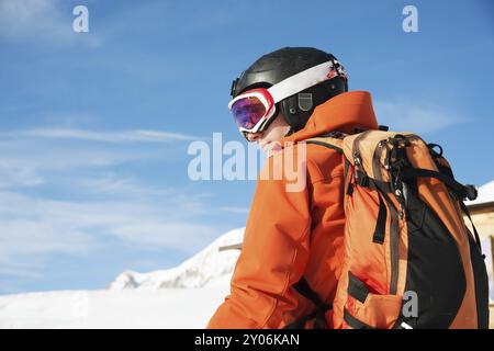 Ritratto di uno sciatore in una tuta arancione con uno zaino sulla schiena in un casco si staglia sullo sfondo di una splendida terra di montagna caucasica Foto Stock