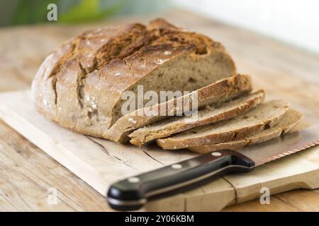 Pane scuro fresco a fette. Tagliere e tavolo in legno, coltello Foto Stock