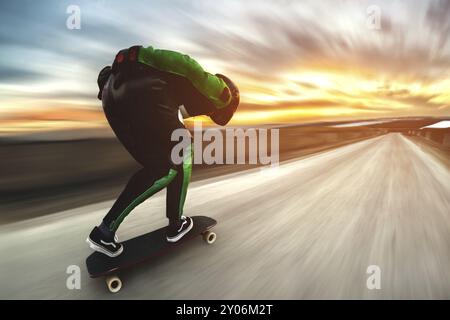 Un uomo con casco e tuta in pelle, in una speciale cremagliera ad alta velocità, cavalca su una lunga longboard per scendere in discesa a galla sullo sfondo di un beauti Foto Stock