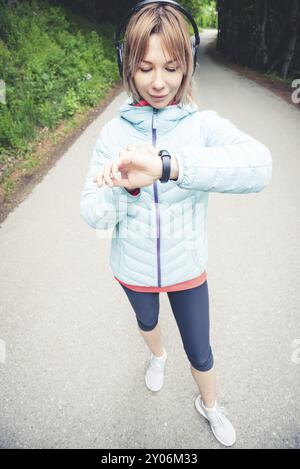 Giovane donna che guarda il suo orologio intelligente mentre si prende una pausa dagli allenamenti sportivi. Donna sportiva che controlla il polso sul dispositivo di orologio intelligente fitness in Foto Stock
