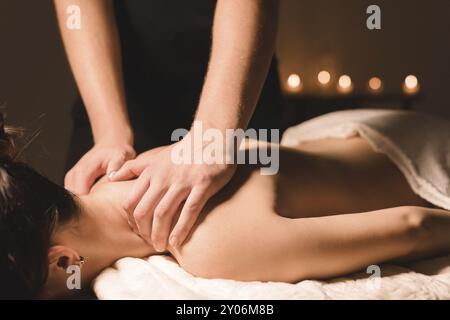 Le mani degli uomini fanno un massaggio terapeutico al collo per una ragazza sdraiata su un lettino massaggiante in una spa con illuminazione scura. Primo piano. Tasto scuro Foto Stock