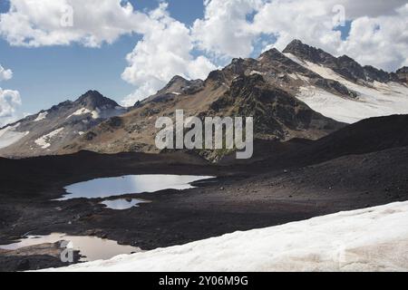 Paesaggio di alta montagna di un lago vulcanico di montagna sulle pendici del vulcano Elbrus addormentato con alte montagne e montagne innevate in estate Foto Stock