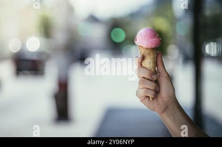 Donna detiene il gelato alla fragola in mano, soleggiata giornata estiva, sfondo sfocato Foto Stock