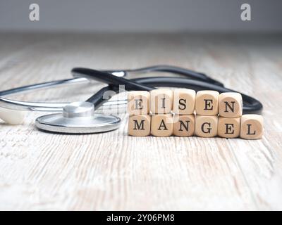 Le parole tedesche la carenza di ferro su piccoli blocchi di legno con uno stetoscopio su un tavolo, assistenza sanitaria o concetto medico Foto Stock