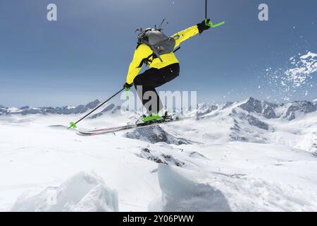 Uno sciatore con attrezzatura sportiva completa salta nell'abisso dalla cima del ghiacciaio sullo sfondo del cielo blu e del Caucaso innevato Foto Stock