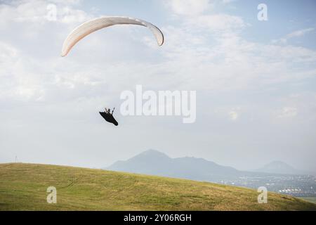 Un parapendio bianco-arancio vola sul terreno montuoso Foto Stock