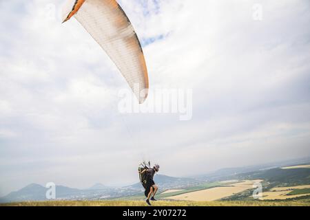 Un parapendio uomo che si decollerà dal bordo della montagna con i campi sullo sfondo. Sport di parapendio Foto Stock