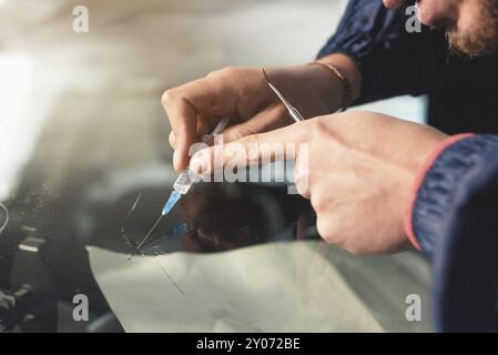 Il primo piano di un riparatore professionista del parabrezza riempie una crepa nel vetro con uno speciale polimero attraverso una siringa. Eliminazione delle incrinature e. Foto Stock