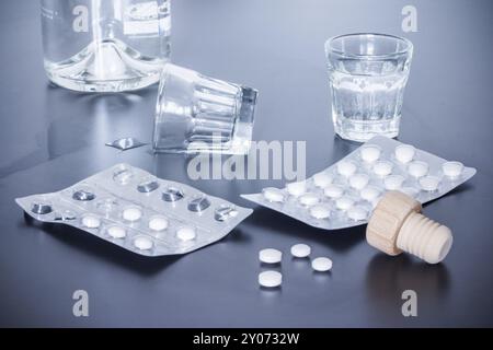 Pillole e alcol su un tavolo grigio. Concetto di abuso di droga Foto Stock