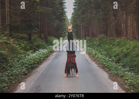 Donna acrobatica con leggings neri e camicia a quadri esegue un cartoncino su un sentiero nella foresta nel mezzo di una foresta profonda. Formazione di coordinamento e agilità Foto Stock