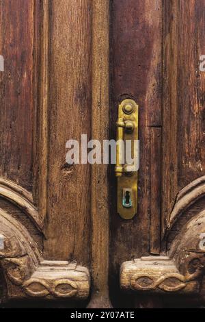 Sfondo vintage. Vecchia maniglia in ottone con elementi di una porta in legno intagliato decorata con massiccia tessitura in legno. Un vecchio concetto di o Foto Stock