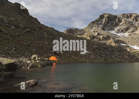 Paesaggio notturno di un lago di alta montagna in un arcipelago nel Caucaso settentrionale con una luminosa tenda turistica sulla riva del lago. Lago ad alta quota Foto Stock