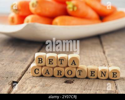 Dadi di legno con le parole il beta-carotene e le carote fresche nel retro, mangiare sano concetto Foto Stock