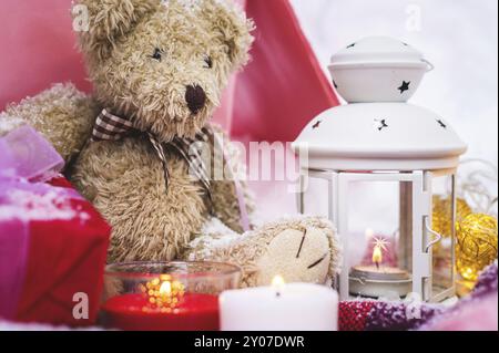 Primo piano di un orsacchiotto con candele di Natale su un accogliente plaid a scacchi all'aperto accanto a una confezione regalo rossa cosparsa di neve. Festività natalizie Foto Stock