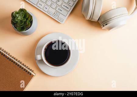 Desktop con blocco note, tastiera per computer, cuffie, piante succulente e tazza di caffè su sfondo beige. Vista dall'alto, disposizione piatta, spazio di copia. Foto Stock