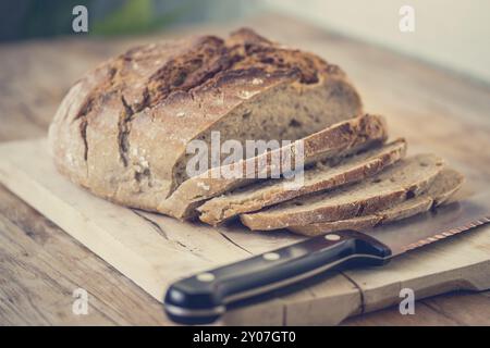 Pane scuro fresco a fette. Tagliere e tavolo in legno, coltello Foto Stock