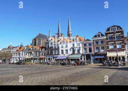 Delft, Paesi Bassi, 8 aprile 2016: Vista colorata sulla strada con tradizionali case olandesi sulla piazza, cupole della chiesa, biciclette, persone che camminano in basso Foto Stock