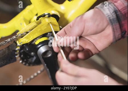 Manutenzione ravvicinata di una mountain bike. Le mani maschio regolano la tensione della catena. Monitoraggio delle condizioni tecniche in officina Foto Stock