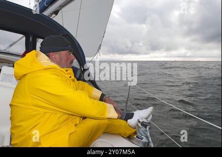 Uomo in pelle d'olio gialla seduto a bordo di uno yacht a vela Foto Stock