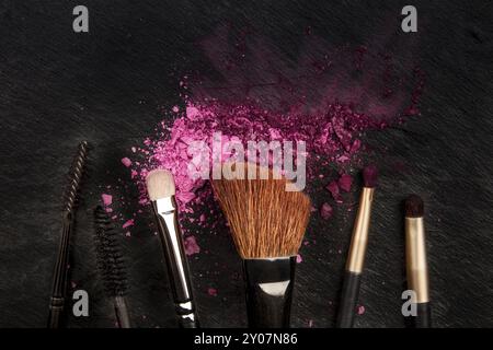 Make-up pennelli con cosmetici frantumato, ripresa dall'alto su uno sfondo nero con un posto per il testo, la bellezza di un modello di progettazione per un banner per il trucco Foto Stock