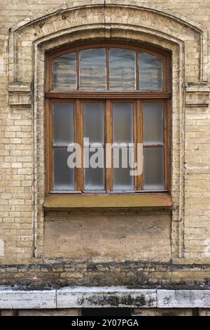 Finestra ad arco vintage nella parete di mattoni gialli. Vetro nero in una cornice in legno rosso scuro marrone. Il concetto di antica architettura vintage in costruzione Foto Stock