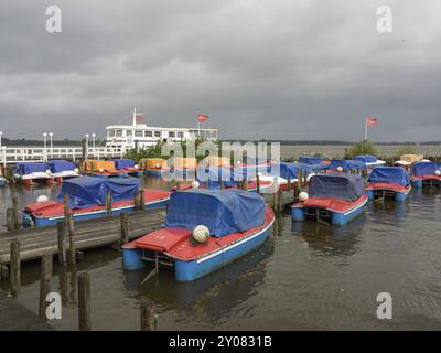 Barche nel porto con il tempo nuvoloso, ormeggio al molo di legno, con bandiere sullo sfondo, Bad Zwischenahn, ammerland, germania Foto Stock