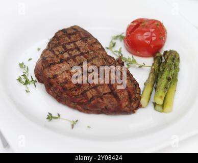 Bistecca di manzo con asparagi cotti e pomodoro su piatto bianco Foto Stock