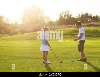 Casual i bambini in un campo da golf holding club di golf. Tramonto Foto Stock