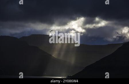 I raggi del sole si infrangono attraverso le spesse nuvole sulla linea costiera delle Isole Faroe Foto Stock